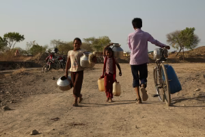 Locuitori ai unui sat din Maharashtra, India, zâmbind în lumina caldă a soarelui în timp ce cară apă, în ciuda provocărilor aduse de secetă. Sursa foto:Gyan Shahane/Unsplash