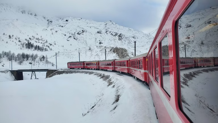 Tren roșu traversând un peisaj acoperit de zăpadă, în Elveția. Sursa foto: Hasmik Ghazaryan Olson/Unsplash